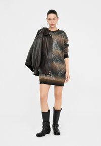 Abito a maglia con una sfumatura di marrone e nero, decorato con pailettes, abbinato a una giacca di pelle scura e stivali neri al ginocchio.