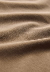 Beežist puuvillane kangas pehme ja sileda tekstuuriga. Kangas on veidi kortsus ning kogu ulatuses on näha õrn põimingumuster.