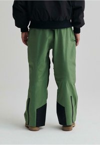 Pantaloni da neve verdi con accenti neri, realizzati in materiale impermeabile, dotati di tasche laterali e zip nella parte inferiore delle gambe per una maggiore regolabilità.