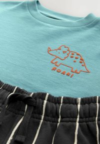 Turkusowa koszulka z krótkim rękawem z pomarańczowym grafiką dinozaura i napisem "ROAR!", połączona z czarnymi szortami w paski z elastycznym pasem.