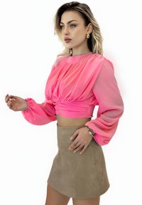 Pink silk blouse with long, puffed sleeves and gathered front detail, paired with a beige suede mini skirt. Simple gold earrings accent the outfit.