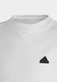 Camiseta de algodón blanca con cuello en V acanalado y un pequeño logotipo de goma negro de Adidas en el lado izquierdo del pecho. Textura suave y diseño sencillo.