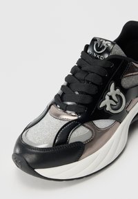 Zwarte en zilveren sport schoen met een mix van gladde en gestructureerde materialen, met een opvallend logo en zwarte veters.