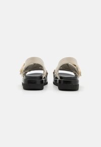 Sandales beige avec une plateforme noire brillante, dotées d'une large bande, d'une sangle ajustable et d'un détail en boucle dorée.