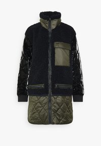 Fleece-fodrad jacka med hög krage, vadderade svarta ärmar, gröna accenter, dragkedjefront och två dragkedjefickor på framsidan.