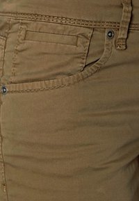 Beige byxor i bomull med en slät textur, med en framficka, diskret sömnad och en liten metallknapp som detalj.