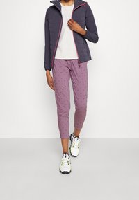Purple patterned pants, light gray shirt, and a dark quilted jacket with pink accents, completed with white and neon running shoes.