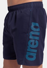 Shorts da nuoto in navy con vita elasticizzata, caratterizzati da un logo "arena" blu a pois sul lato e una superficie di tessuto liscia.