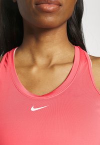 Pink atletisk tanktop lavet af glat stof med en scoop halsudskæring og hvid Nike-logo på brystet. Den har spaghetti-stropper.