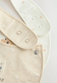 Beige og creme babydragter med trykknapper, stjernemønstre og en indsyet plysdyret detalje. Blød, bomuldsstof struktur.
