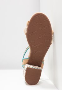 Brązowe sandały na platformie z turkusowymi paskami i plecioną fakturą. Posiadają gumową podeszwę z powtarzającym się wzorem logo. Widok od dołu.