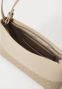Beige håndveske med teksturert bunn og glatt topp. Har glidelåslukking, innvendige lommer og Calvin Klein-merke.