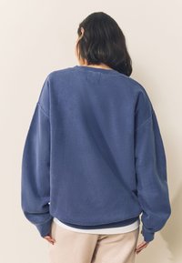 Blauwe fleece trui met verlaagde schouders, geribde manchetten en zoom. Zachte textuur, ontspannen pasvorm, met een ronde hals en minimale naden.