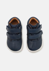 Marineblaue Lederschuhe mit zwei Klettverschlussriemen, abgerunderter Spitze und beigem Innenfutter, die auf einer weißen Gummisohle ruhen.
