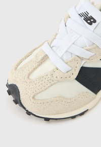 Beige og hvit sneaker med teksturert semsket overdel, meshpaneler, hvite lisser og en svart aksentstripe, med en gummisåle.