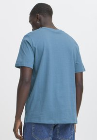 Kortærmet t-shirt i blå bomuld, set bagfra. Klassisk rund halsudskæring, afslappet pasform, glat tekstur, med slidser i siden ved kanten.