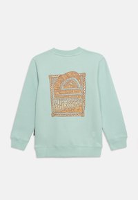 Φουτεράκι μακρυμάνικο σε ανοιχτό γαλάζιο με μεγάλο πορτοκαλί και λευκό αφηρημένο γραφικό και στυλιζαρισμένο κείμενο στην πλάτη.