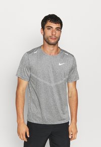 Camiseta gris de manga corta de Nike con cuello redondo, que presenta una textura sutil y un acento del logo blanco en el pecho y los hombros.