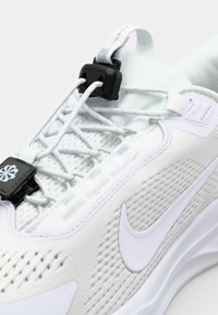 White athletic shoe with mesh upper, textured panels, elastic laces, and a black locking mechanism. Features a white swoosh logo.