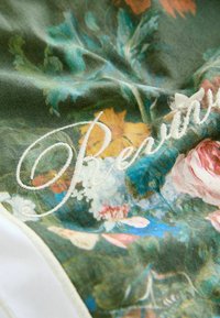 Rohelise taustaga lillelise mustriga kangas, millel on embroideritud valged tekstid. Kaunistatud roosa, kollase ja sinise lilledega; pehme tekstuur.