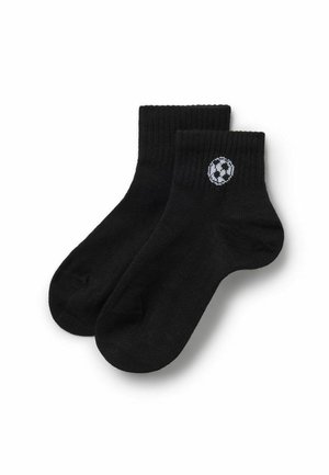 Une paire de chaussettes noires courtes avec un petit motif de ballon de football blanc et noir près du bord supérieur d'une chaussette.