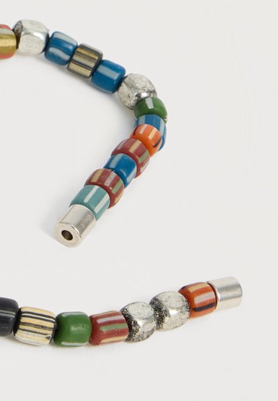 Κολιέ με χάντρες κυλινδρικές, στρογγυλές και μεταλλικές σε μπλε, πράσινο, κόκκινο, πορτοκαλί, μαύρο και ασημί, τοποθετημένες σε χοντρή καμπύλη σε λευκό φόντο.