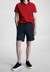 Czerwona koszulka polo z kontrastowym kołnierzykiem, połączona z granatowymi szortami kąpielowymi z elastycznym paskiem w talii. Całość uzupełniają czarne trampki.