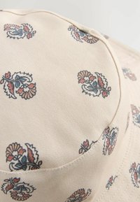 Beige bucket hat gemaakt van gestructureerde stof, met een bloemenpatroon in blauw en roze. Ronde kroon met een gestikte rand.