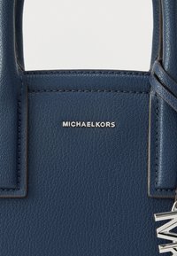 Ciemnoniebieska skórzana torebka z wytłoczonym logo "MICHAELKORS." Posiada solidne uchwyty i srebrne metalowe elementy. Powierzchnia o fakturze.