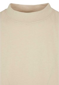 T-shirt beige à col rond montrant seulement le haut de la poitrine et le col avec des coutures visibles sur le tissu.