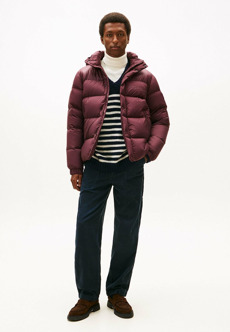 Maroon puffer jacket with a hood, elastic cuffs, and a glossy finish, worn over a striped sweater and dark corduroy pants. Brown loafers.