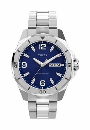 Montre en acier inoxydable avec un cadran bleu, de grands marqueurs d'heure blancs, un affichage de la date et un bracelet argenté. Elle présente une résistance à l'eau et un design audacieux.