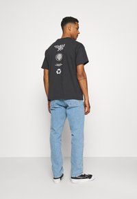 Camiseta de algodón negra con gráficos impresos en la parte trasera, combinada con jeans azul claros y zapatillas negras. Diseño simple y de corte relajado.