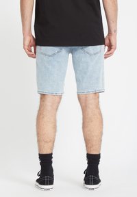 Lysblå denimshorts med lige skæring og flosset kant, parret med sorte sokker og sorte sko, set bagfra.