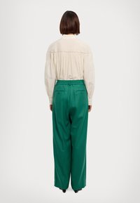 White button-up shirt with intricate pleating at the back, paired with loose-fitting green trousers featuring a drawstring waist and pockets.