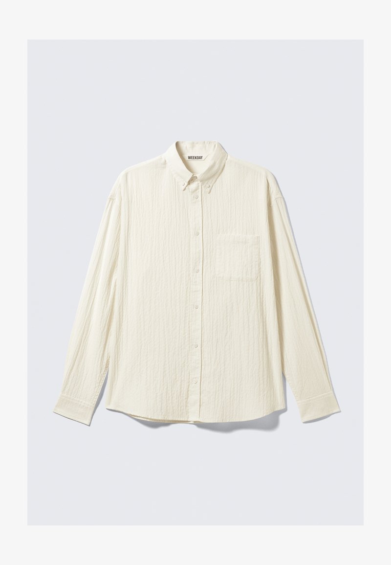 Chemise blanche texturée à manches longues, avec un col boutonné et une poche poitrine unique. Étiquette de la marque "WEEKDAY" visible à l'intérieur du col.