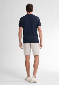 Námořnické pletené tričko s krátkými rukávy, spárované se světle béžovými pruhovanými šortkami. Model v bílých tenisových botách, viděný zezadu.