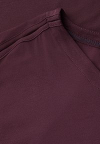 T-shirt bordeaux à manches courtes avec un col en V. Texture lisse avec des détails de couture le long de l'encolure et de l'ourlet. Tissu doux.