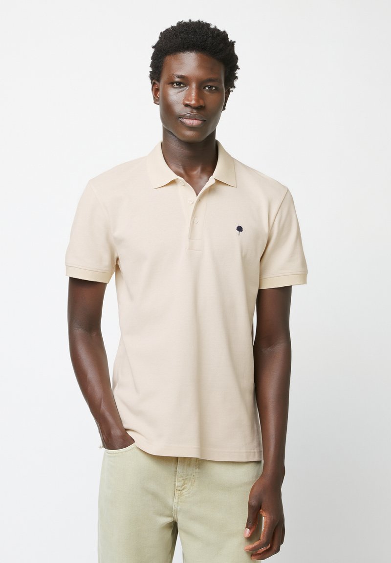 Polo beige in cotone, con un piccolo logo a forma di albero blu navy sul petto, maniche corte e un classico design del colletto.