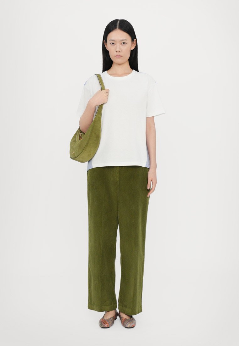 T-shirt blanc à manches courtes, pantalons en velours côtelé verts olive et chaussures à enfiler rayées multicolores. Le sac est en daim olive avec un design incurvé.