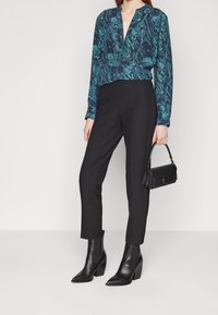 Långärmad, marinblå skjorta med abstrakta gröna mönster, parat med skräddarsydda svarta byxor och spetsiga svarta klackstövlar. Inkluderar en liten svart handväska.