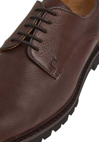 Hnědé kožené společenské boty se šesti černými očky na šněrování, texturovaným svrškem, kontrastním prošíváním a robustní gumovou podrážkou se vzorem vzorku.