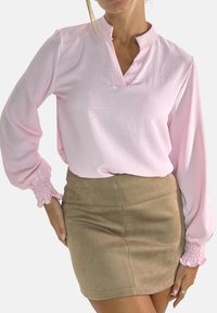 Blusa rosa a maniche lunghe con collo alla coreana e polsini arricciati, abbinata a una minigonna in suede color cammello con una texture liscia.