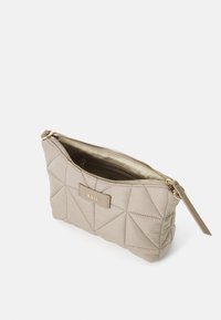 Funda de nylon acolchada beige con un cierre dorado, etiqueta de marca y bolsillo interior, con forma cuadrada y textura suave.