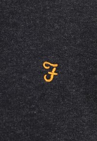 Tessuto grigio scuro con una texture morbida, caratterizzato dalla lettera "F" ricamata in arancione con un font stilizzato al centro.