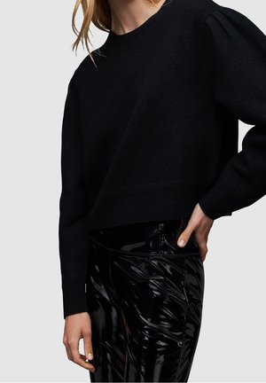 Maglione nero corto con maniche lunghe e scollatura tonda, realizzato in tessuto testurizzato. Abbinato a leggings neri lucidi con finitura liscia.