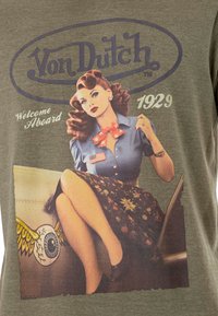 T-shirt vert avec une illustration de style vintage d'une femme en blouse bleue et jupe à motifs, accompagnée du texte "Von Dutch" et "Welcome Aboard 1929."