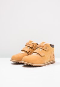 Stivali ankle in suede color sabbia con due strap in velcro, fodera morbida, suola in gomma e dettagli con il logo Timberland sul lato.