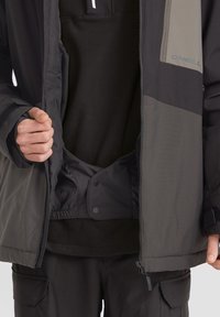 Chaqueta aislante para hombre, negra y gris oscuro, con cierre de cremallera frontal, cintura elástica y cierre a presión. Tejido suave con bolsillos interiores.