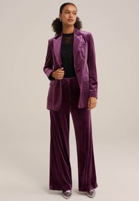 Paarse fluwelen pak met een getailleerde blazer en wijde broekspijpen, gecombineerd met een zwart kanten top. Glad oppervlak en scherpe revers.